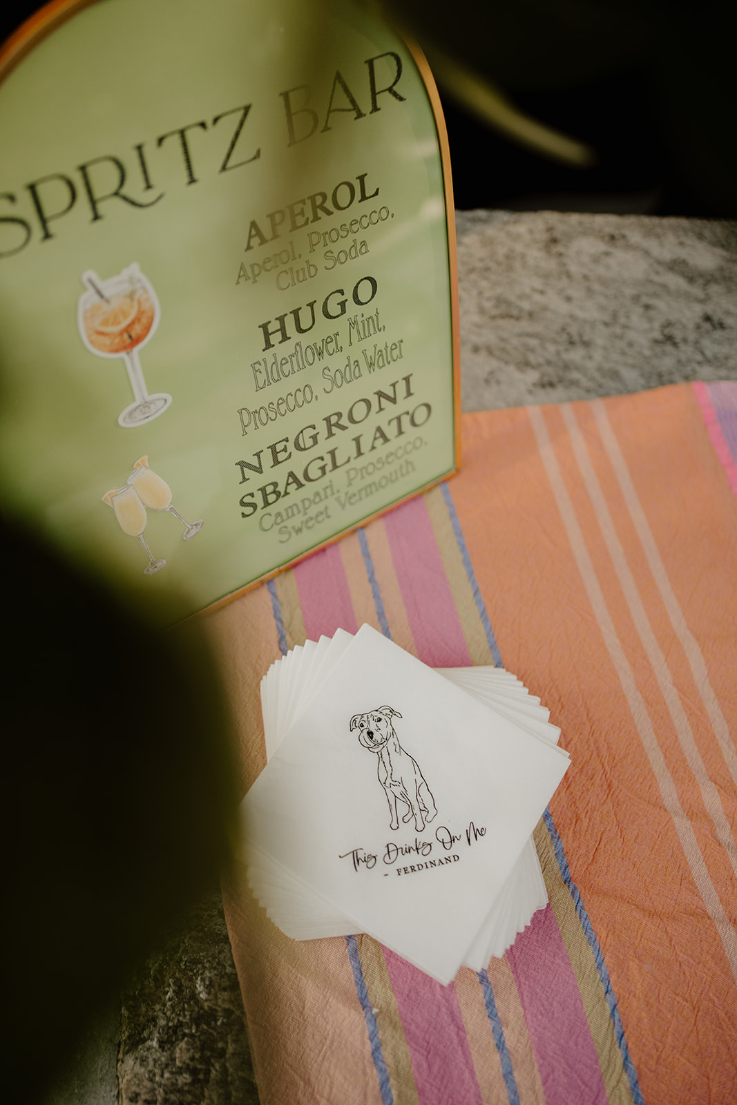 Custom napkins featuring a dog illustration next to a green Spritz Bar menu on a striped runner.
